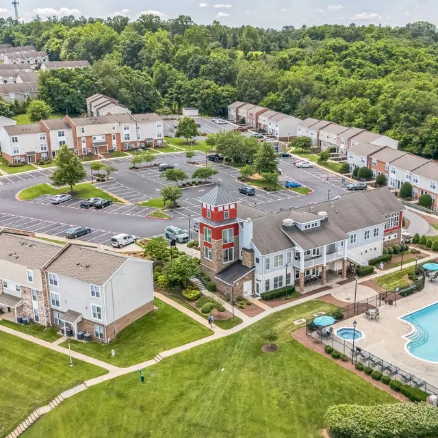 Aerial View of Residential Community Aerial view of a residential community featuring apartment buildings, parking spaces, and a swimming pool surrounded by greenery.