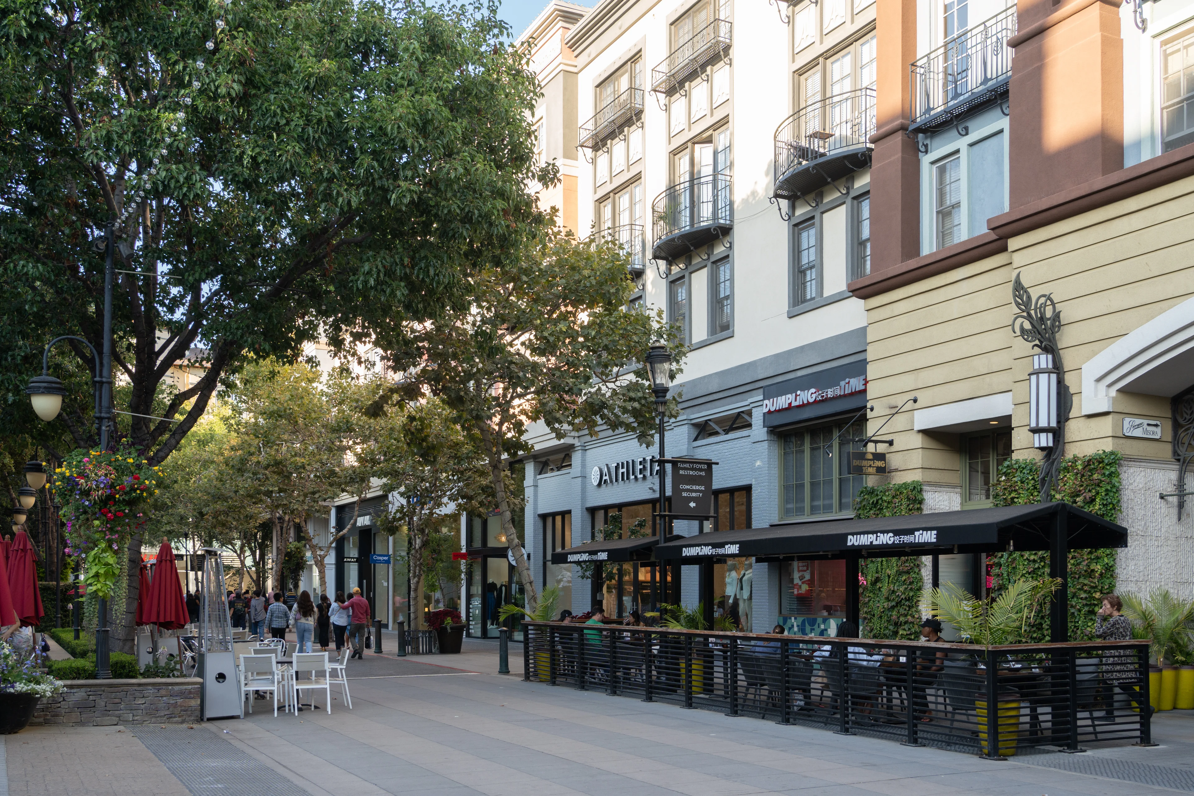 Urban Street Scene with Shops and Outdoor Dining A lively urban street scene with shops and outdoor dining areas, featuring trees and decorative lights.