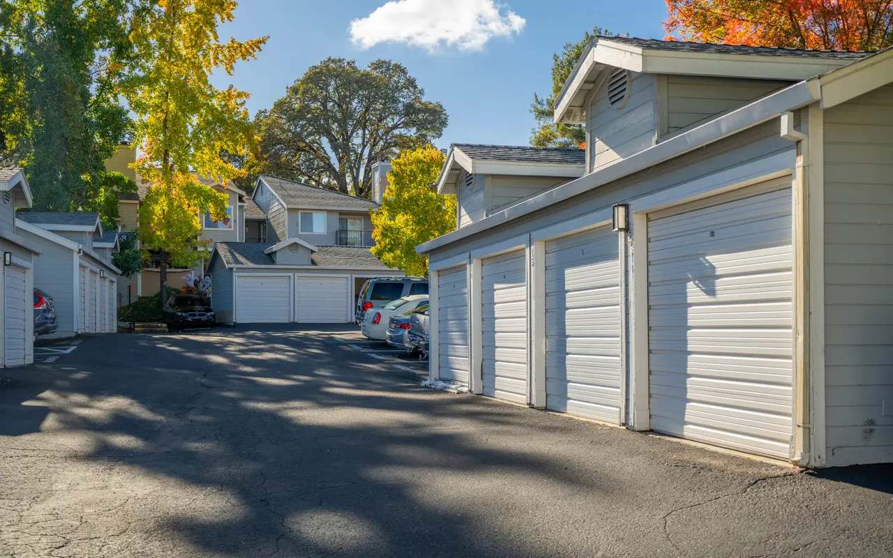 Photo of a residential parking lot featuring garages and colorful autumn foliage in nearby trees.