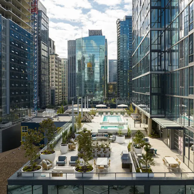 Aerial view of a modern urban landscape featuring a rooftop pool surrounded by high-rise buildings and green plant life.