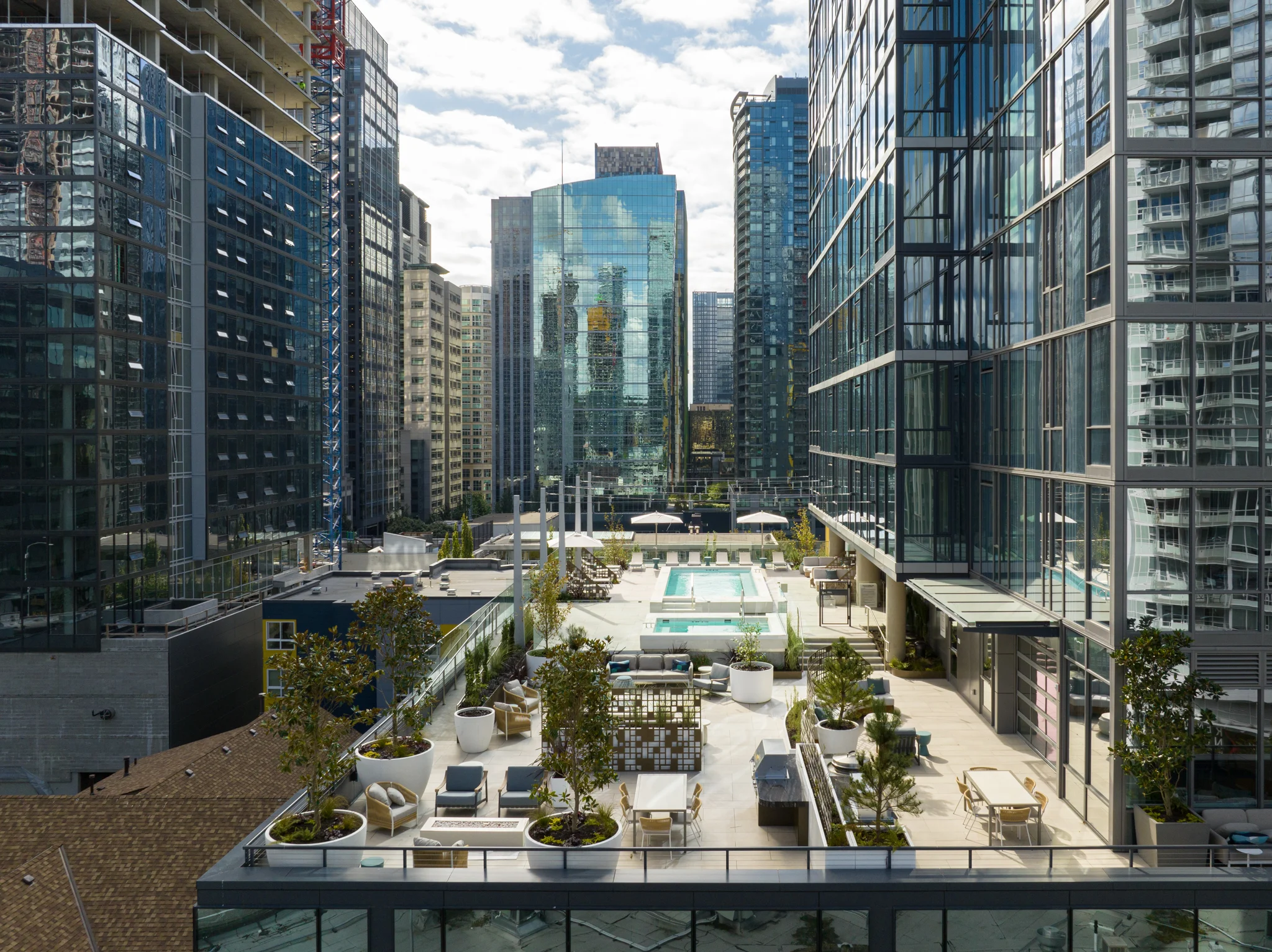 Aerial view of a modern urban landscape featuring a rooftop pool surrounded by high-rise buildings and green plant life.