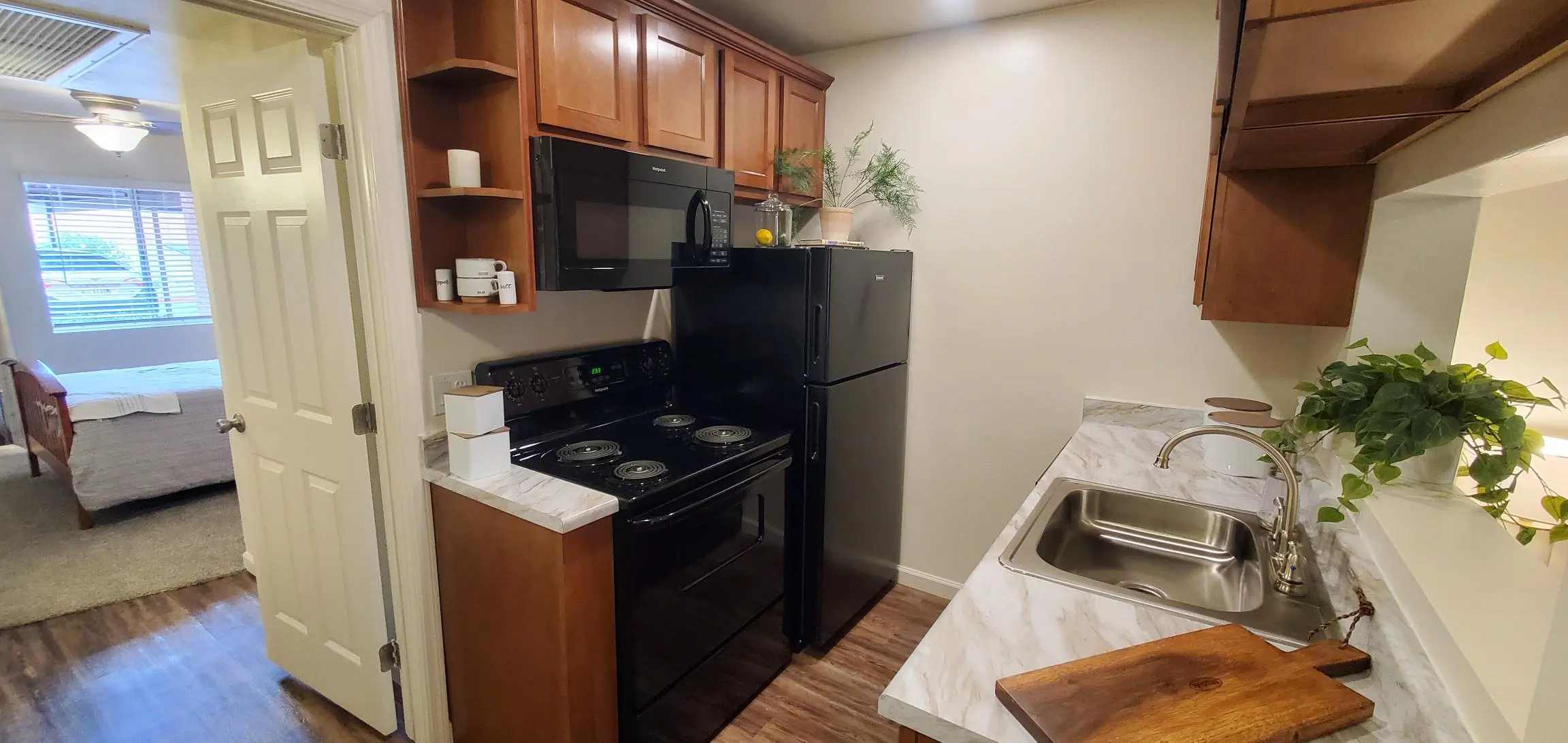 Modern Apartment Kitchen A modern kitchen in an apartment featuring dark wood cabinets, black appliances including a stove and refrigerator, and a sink with a marble countertop. In the background, there is a glimpse of a living space.