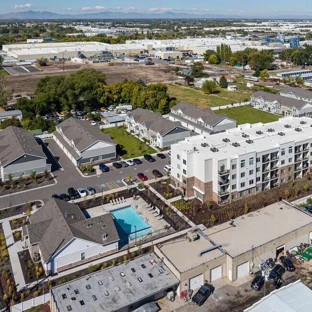 Aerial view of a residential complex featuring multiple buildings and a swimming pool, surrounded by greenery and parking spaces.