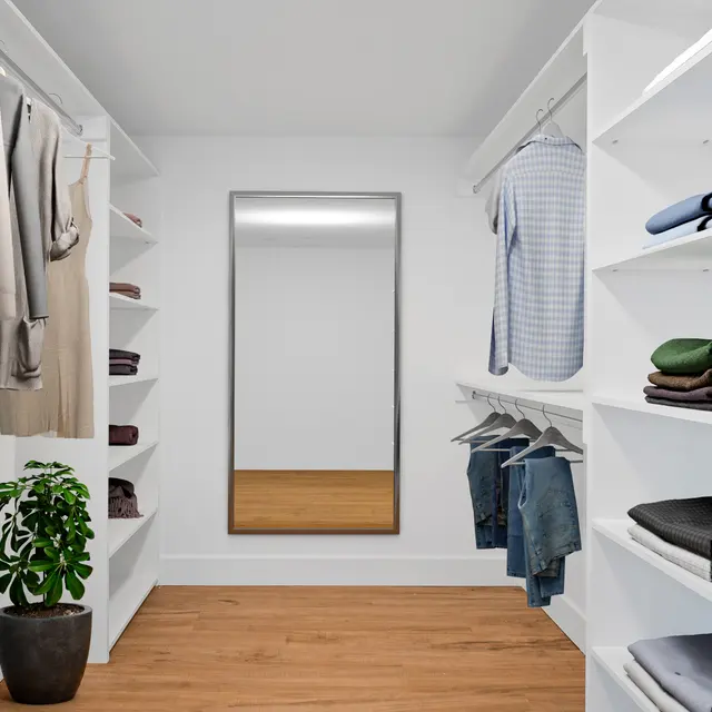 A spacious and organized walk-in closet featuring hanging clothes, shelves with neatly folded garments, a large mirror, and a potted plant.