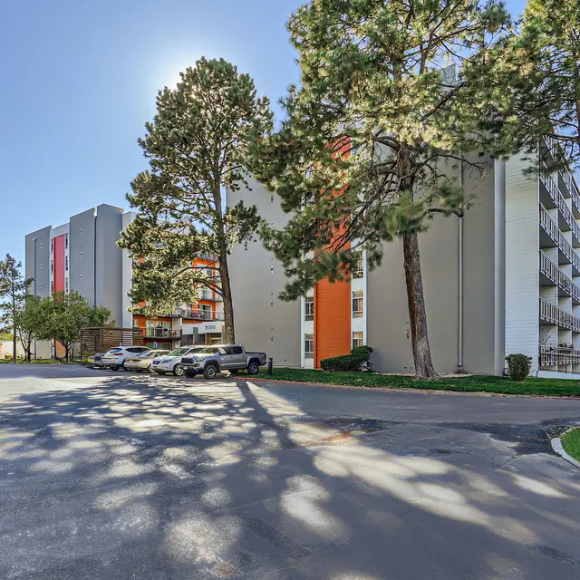 Exterior view of a modern apartment building surrounded by trees and parked cars.