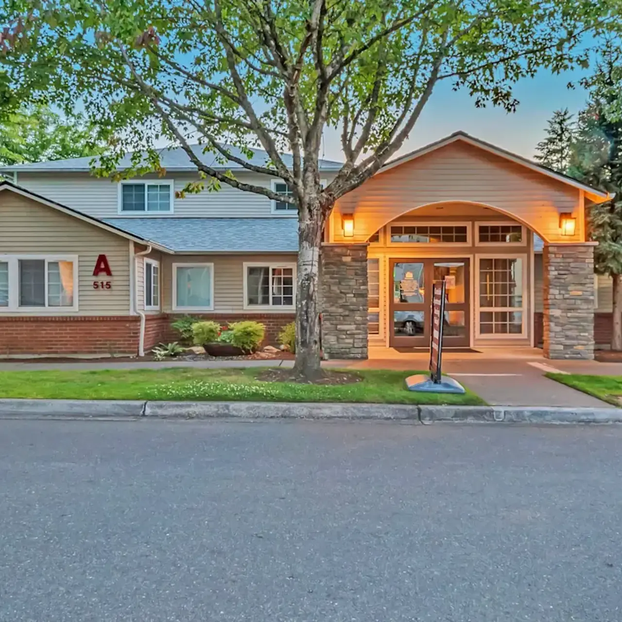 A modern residential building with a welcoming entrance, surrounded by green trees and well-maintained landscaping.