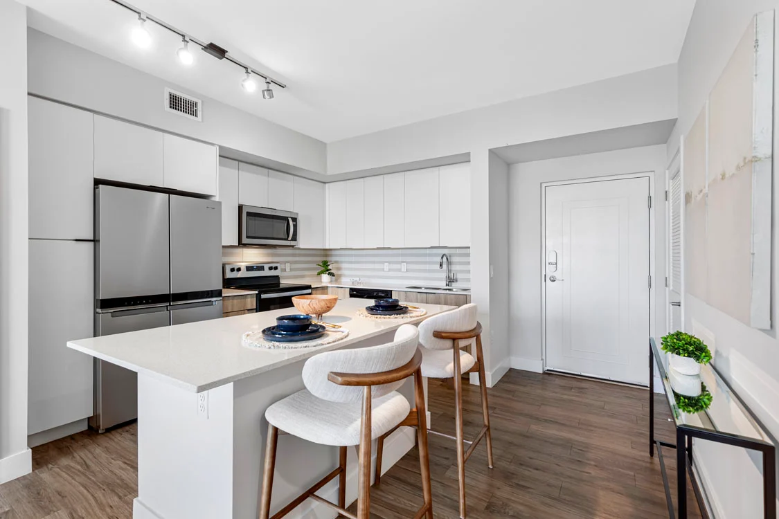 Modern Apartment Kitchen A modern kitchen featuring stainless steel appliances, white cabinetry, and a spacious island with bar seating. The kitchen has a light, airy feel with wooden flooring and minimal decor.