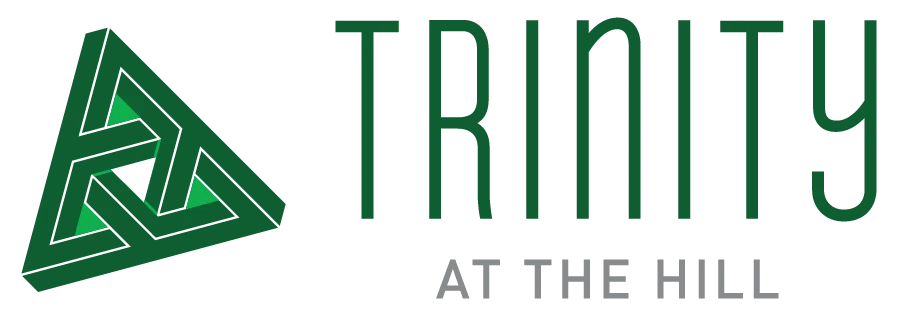 Logo for Trinity at the Hill, featuring a green triangular design with the word 'TRINITY' in bold letters and 'AT THE HILL' in lighter letters.