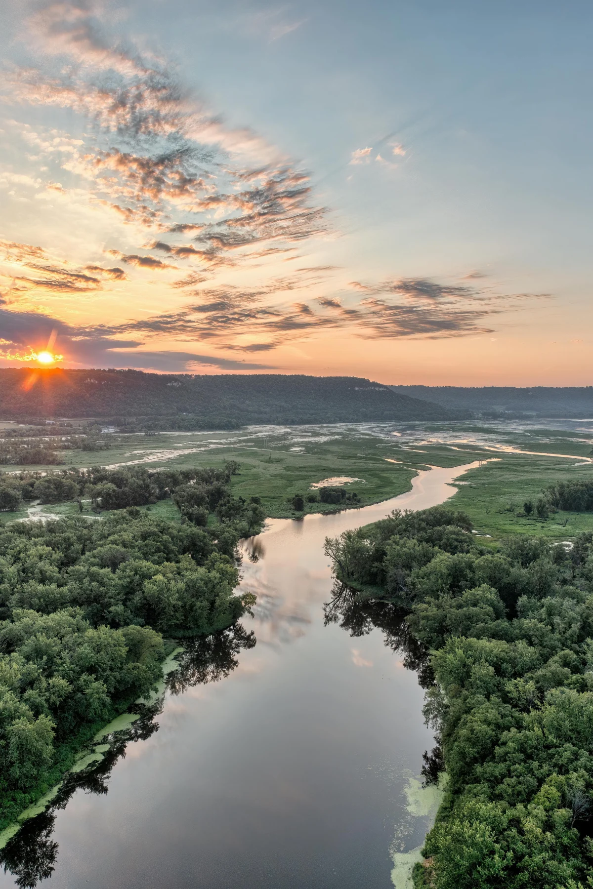 Serene Sunset Over River A picturesque view of a river winding through lush green landscapes during sunset, with a vibrant sky painted in orange and blue hues.