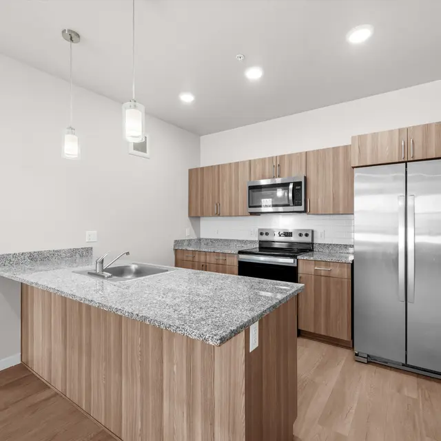 A modern kitchen featuring wooden cabinetry, stainless steel appliances, and a breakfast bar with granite countertops.