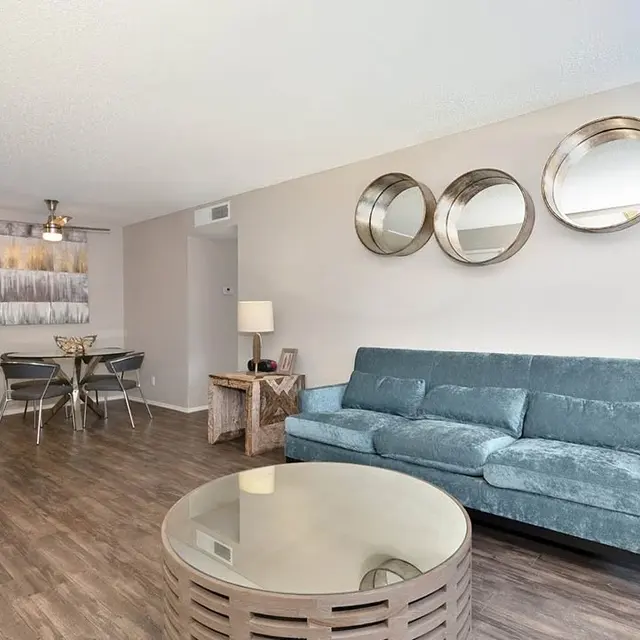 A modern living room featuring a blue sofa, round coffee table, and dining area in the background.