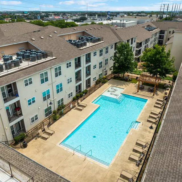 Aerial view of a modern apartment complex featuring a swimming pool surrounded by lounge chairs and greenery.