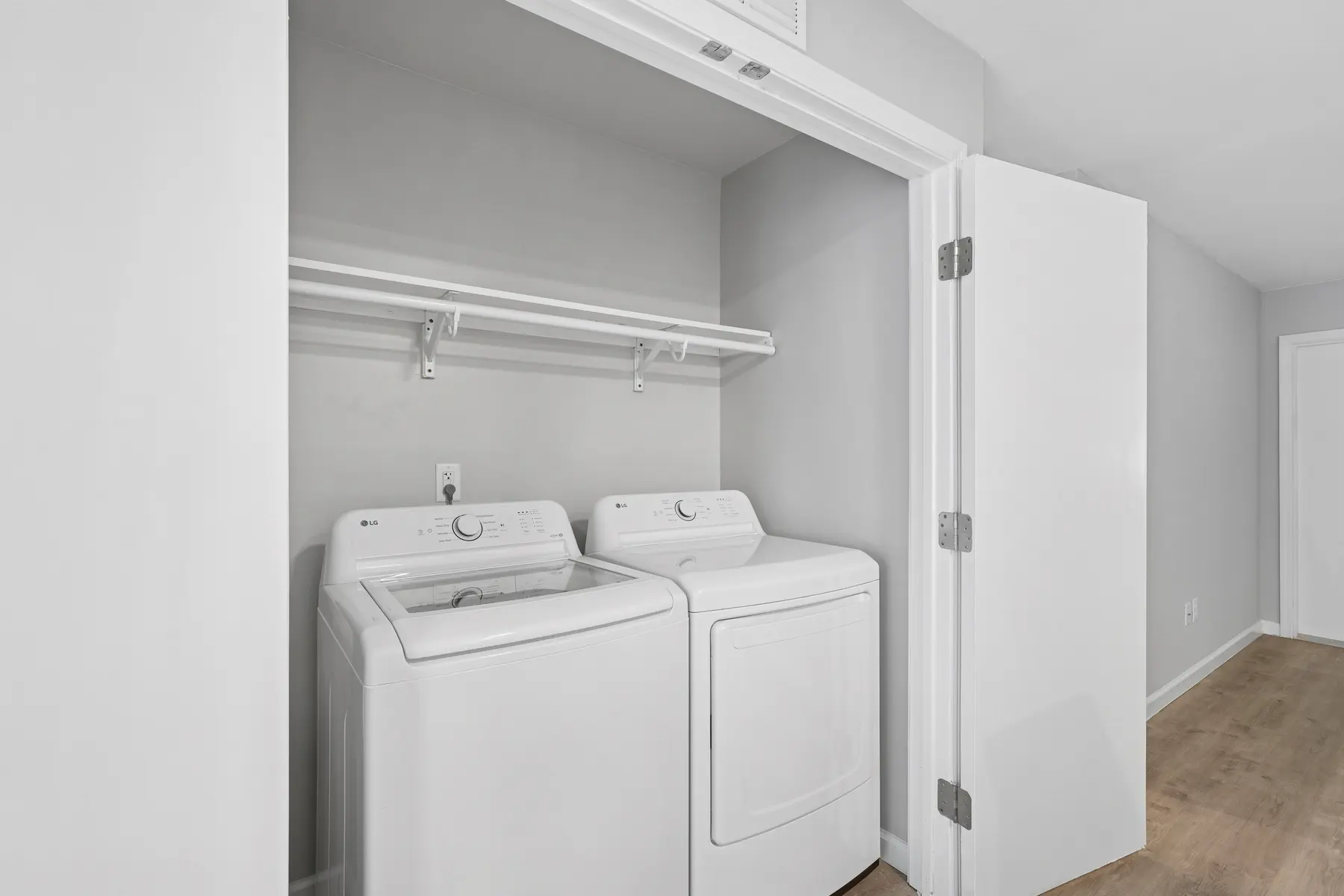 A clean and modern laundry room featuring a washer and dryer side by side, with a shelf above, inside an open closet space.