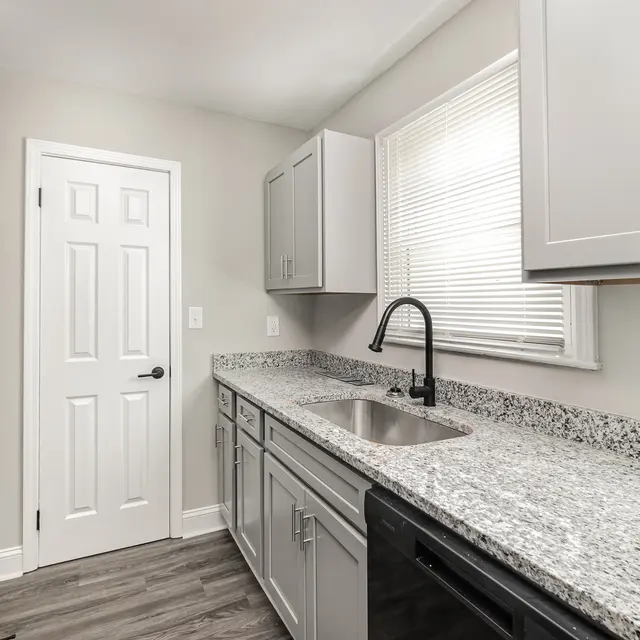 Modern kitchen with gray cabinets, granite countertops, stainless steel sink, and appliances. Bright natural light from window.