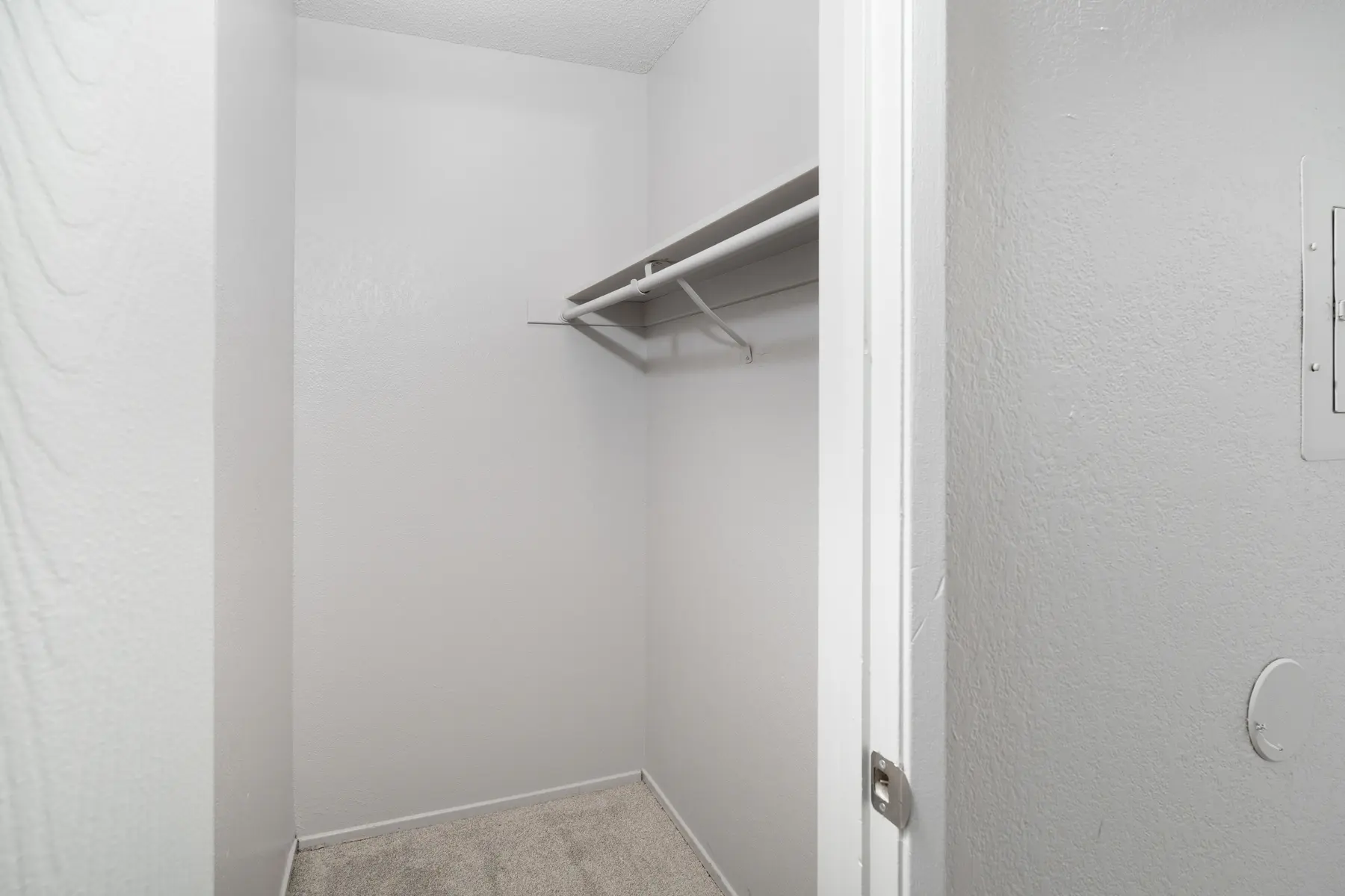 A small empty closet with a bare wall and a single hanging rod.