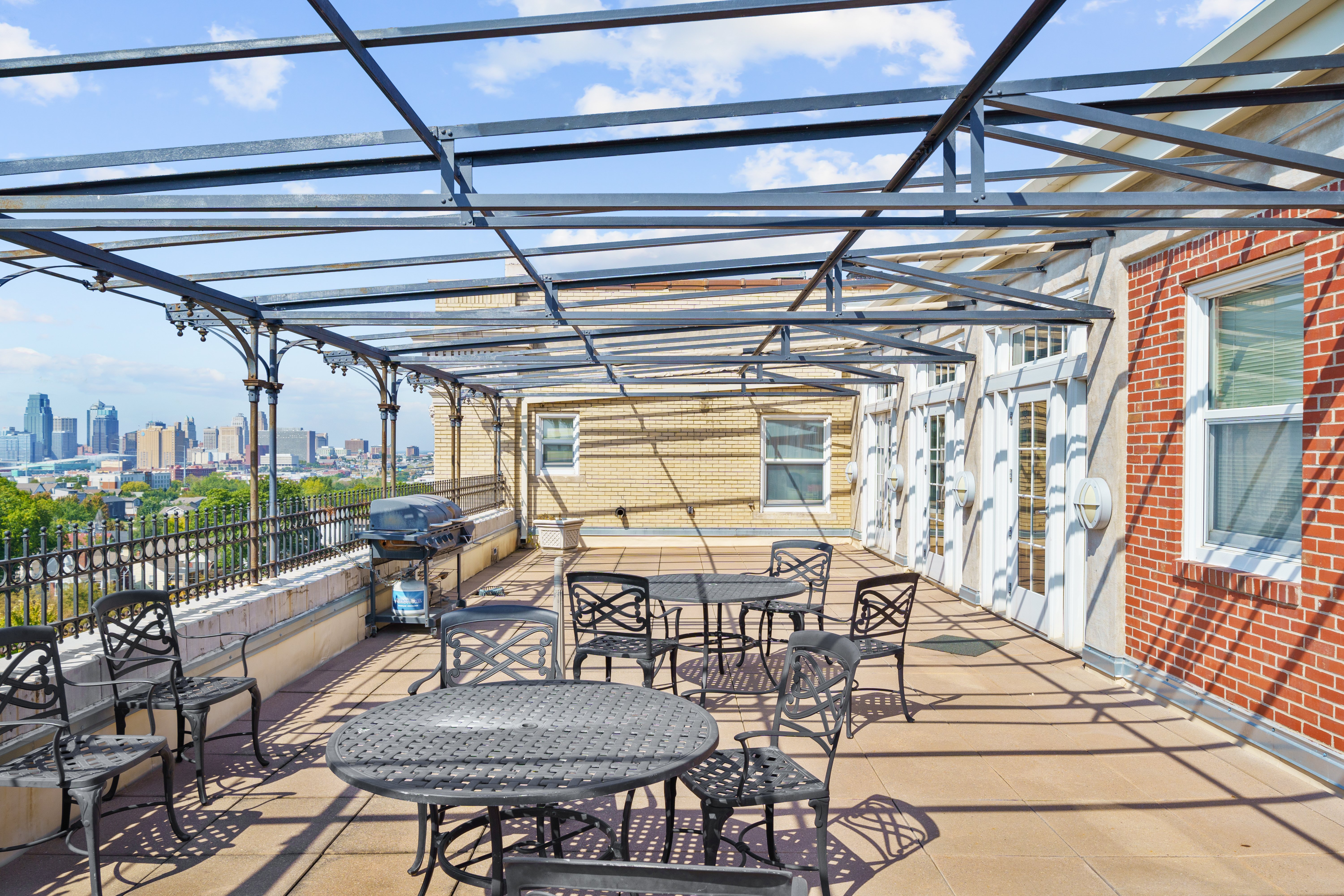 Rooftop Terrace with City View A rooftop terrace with black metal tables and chairs, overlooking a city skyline under a clear blue sky.