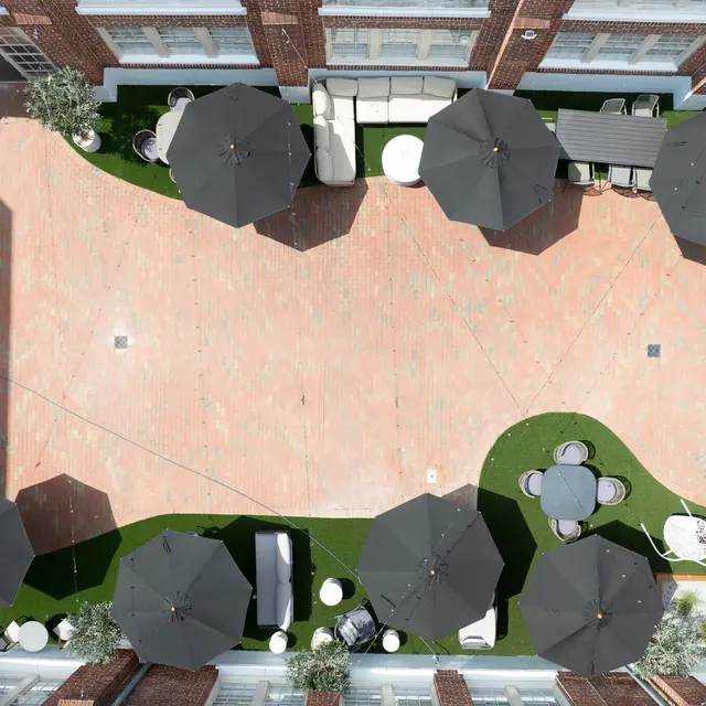 Aerial view of a landscaped outdoor space with several black umbrellas, seating areas, and greenery on a brick-paved patio.