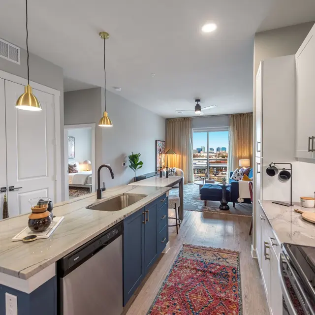 Contemporary Kitchen and Living Room A modern kitchen with a view into a living room area showcasing large windows and a balcony. The kitchen features a sleek design with a central island, stainless steel appliances, and stylish lighting fixtures. A decorative rug adds warmth to the space.