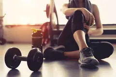 Post-Workout Relaxation A person sitting on a gym floor, resting, with a dumbbell and a water bottle nearby. The lighting is warm and natural, indicating a late afternoon workout vibe.