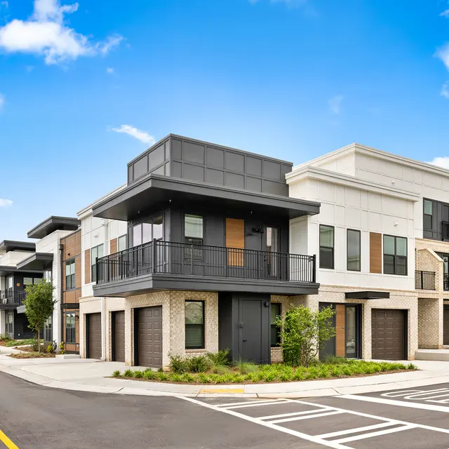 Modern Apartment Complex Street View A modern street view of contemporary apartment buildings, featuring a mix of brick and stucco exteriors, balconies, and wide sidewalks under a bright blue sky with fluffy clouds.