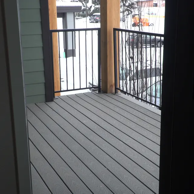 View from inside an apartment looking out onto a covered balcony with a wooden railing and snow-covered surroundings
