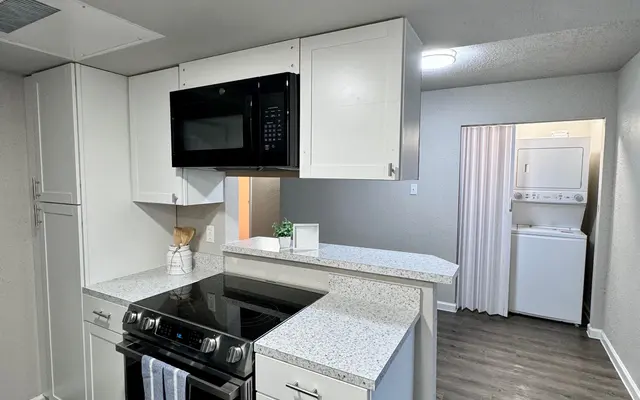 Sleek Modern Kitchen A modern kitchen featuring white cabinetry, a black stove and microwave, and a neutral color scheme. There is a laundry area visible in the background separated by a white curtain.
