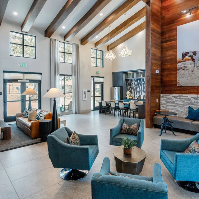 A spacious and modern lobby area featuring stylish seating arrangements, large windows, and wooden beams. The decor includes a mix of contemporary and rustic elements, with artwork on the walls and a cozy atmosphere.