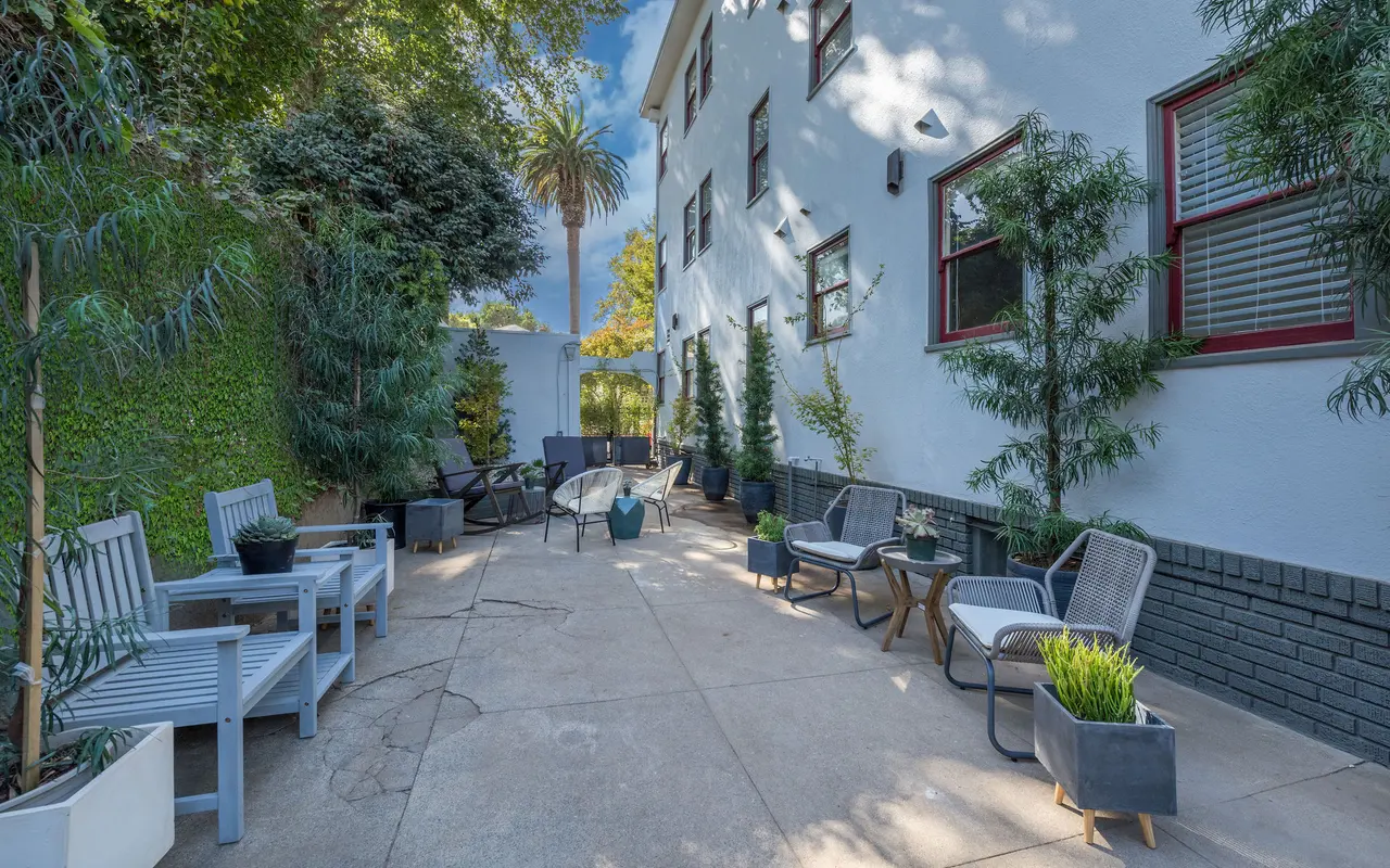 A spacious outdoor living area featuring seating arrangements, greenery, and a well-maintained pathway.