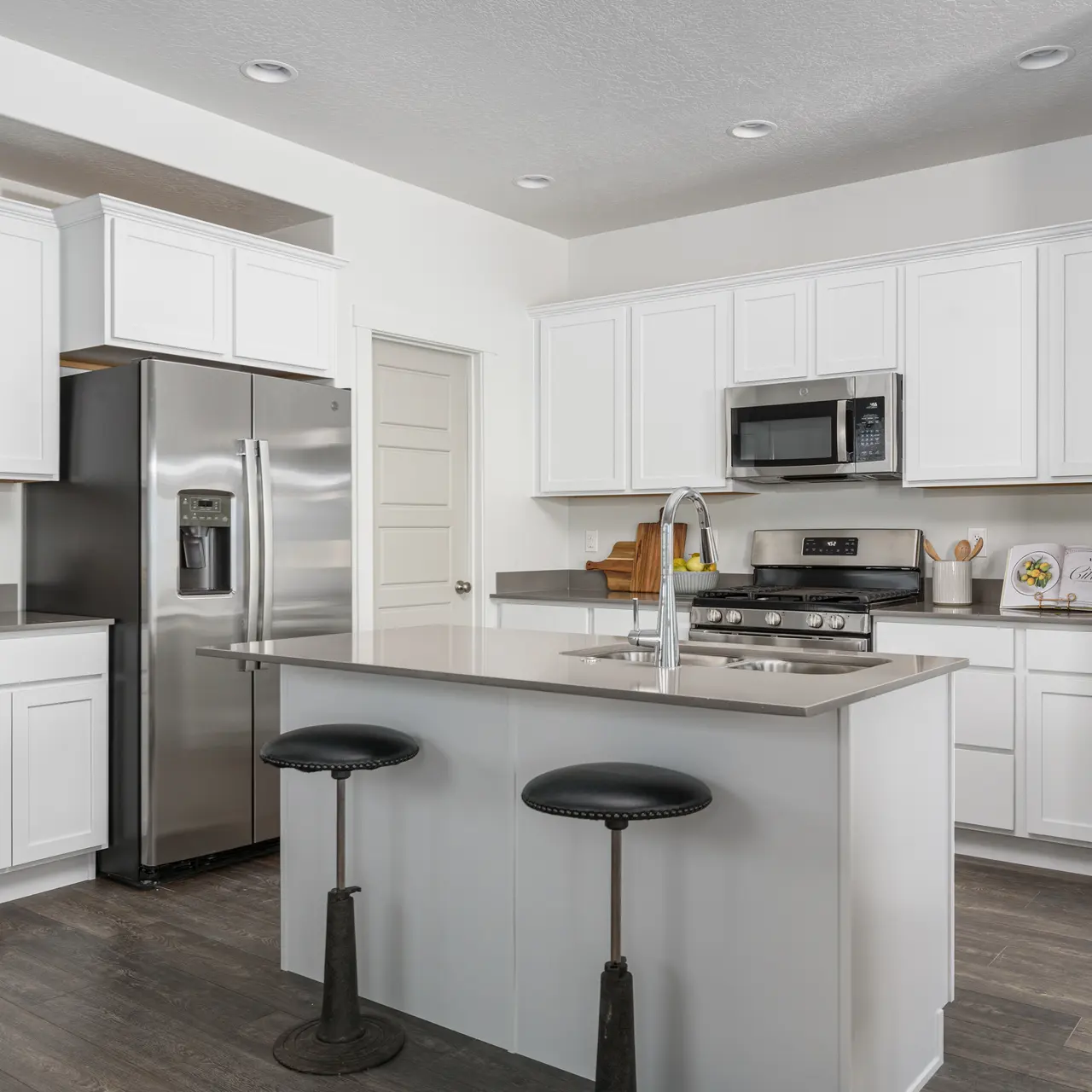 A modern kitchen featuring white cabinetry, stainless steel appliances, and a large island with bar stools.