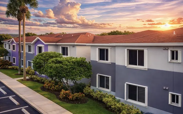 A colorful apartment building during sunset, featuring shades of purple and gray with landscaped greenery in front.