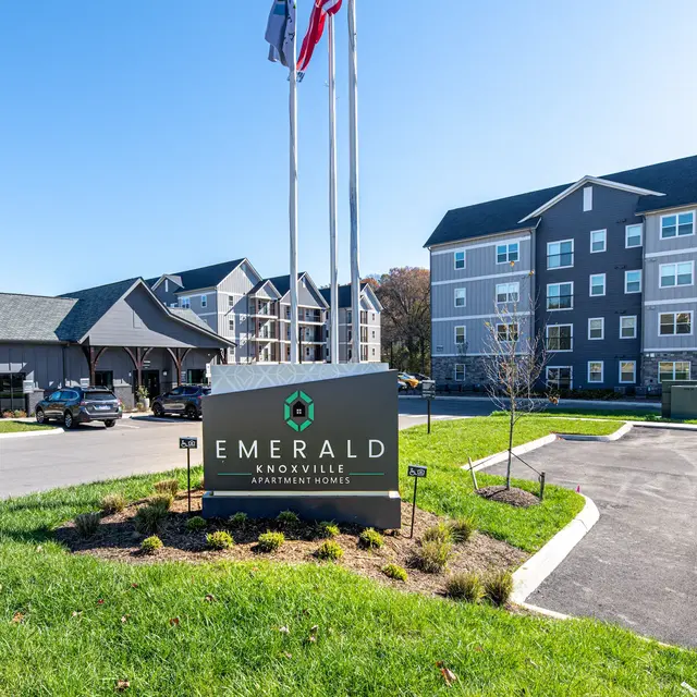 Exterior view of Emerald Knoxville Apartment Homes with sign and flags in foreground.