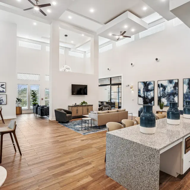 Modern open living space with high ceilings, stylish furniture, large windows, and a communal kitchen area.
