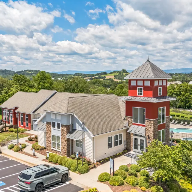 Aerial View of Residential Community with Pool An aerial view of a residential community featuring multiple buildings, a pool, and surrounding greenery under a partly cloudy sky.