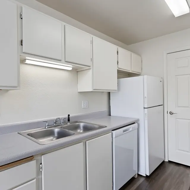 Contemporary Kitchen Design A modern kitchen with white cabinets and appliances, featuring a double sink, a refrigerator, and a door leading to another room.