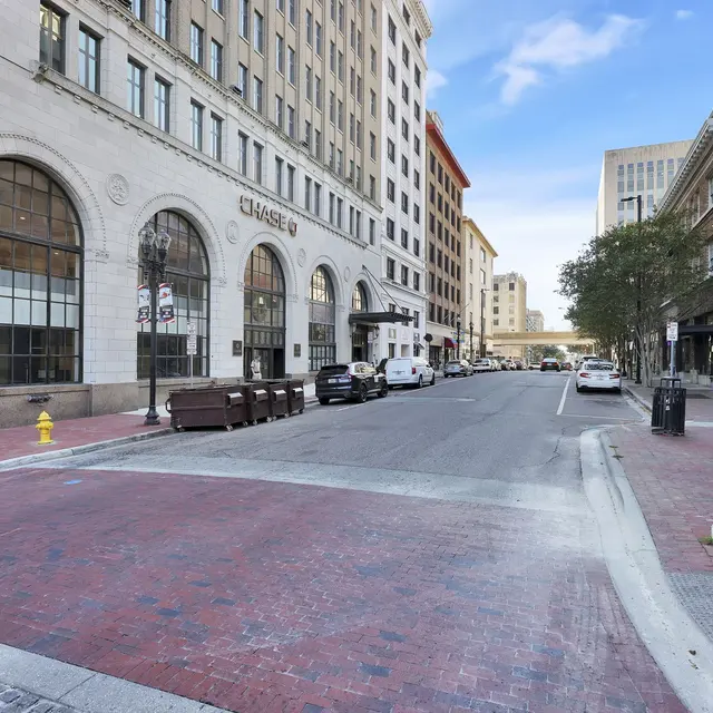 Downtown Street View A city street featuring buildings with varied architectural styles and a crosswalk. The view shows a bank on the left, lined with trees, and parked vehicles along the street.