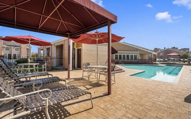 An outdoor pool area featuring lounge chairs, umbrellas, and a view of a building nearby.