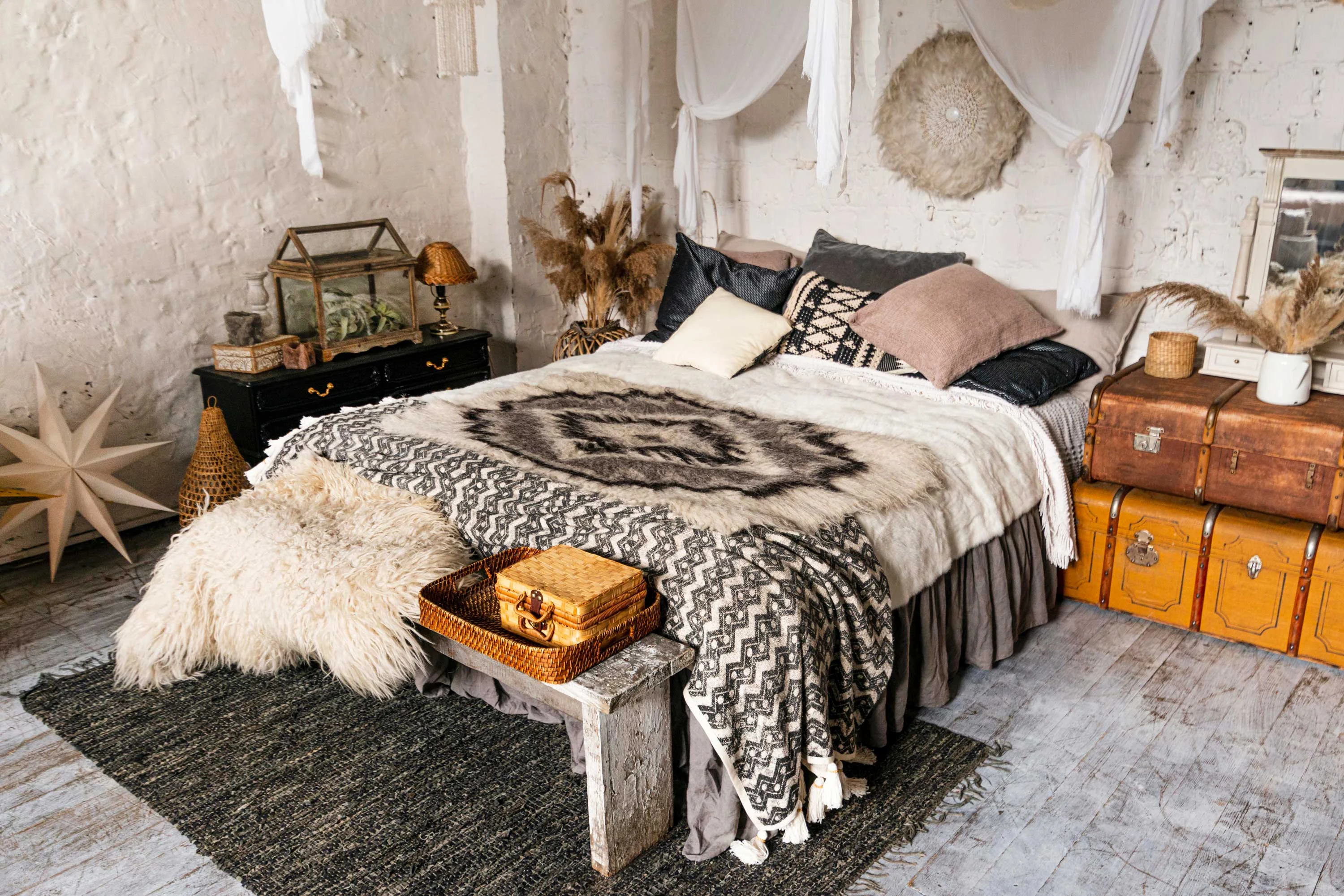 Bohemian Bedroom Interior A cozy bohemian-style bedroom featuring a large bed with patterned blankets, fluffy throws, and decorative pillows. The room has natural light, wooden flooring, and various decorative elements like a lamp, plants, and wooden furniture.