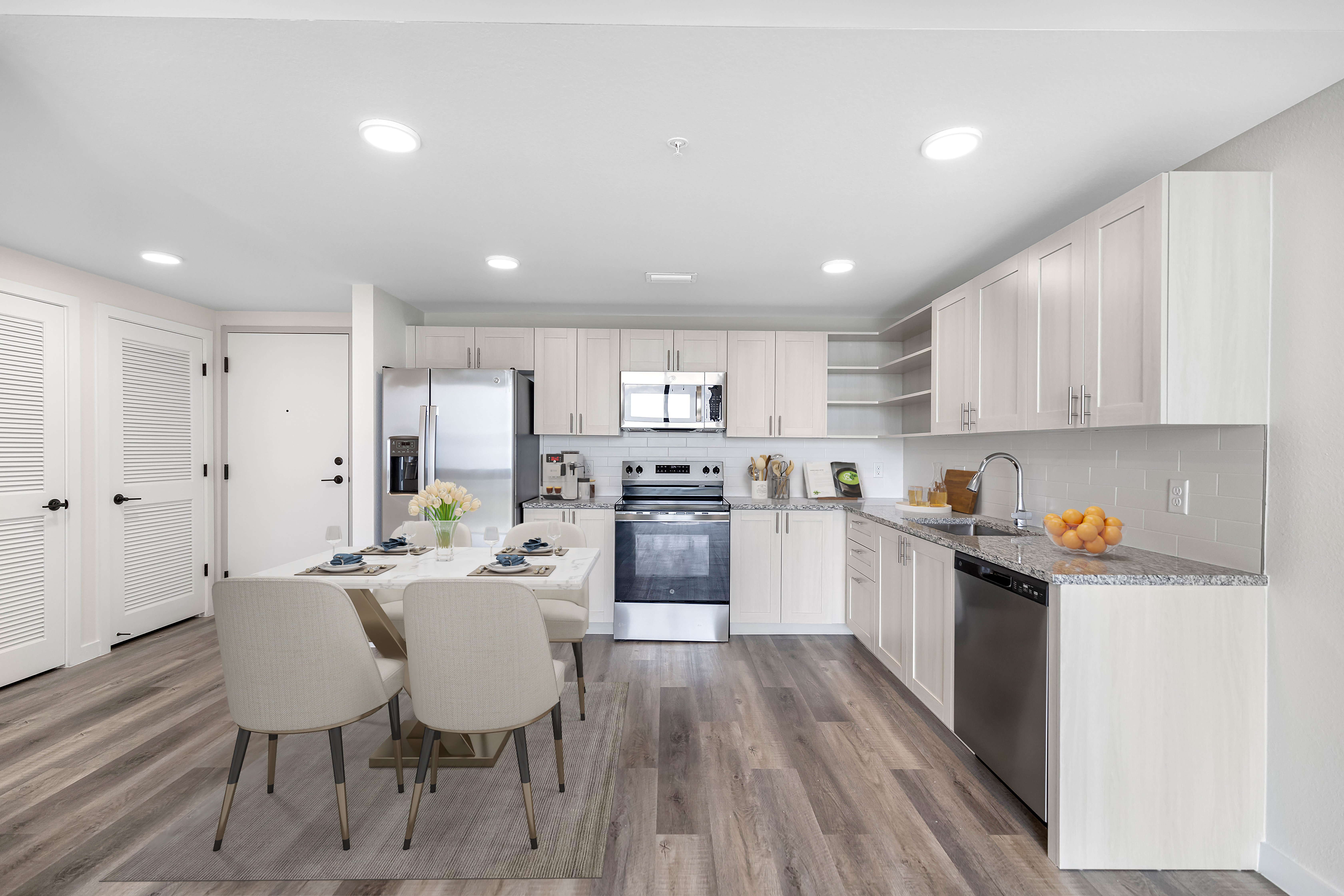 A modern kitchen featuring white cabinets, stainless steel appliances, and a dining area with a table and chairs.