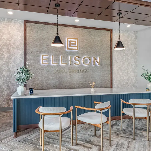 Modern reception area with the name 'Ellison' prominently displayed on the wall. There are several chairs at the reception desk and decorative elements like a plant and diffuser.
