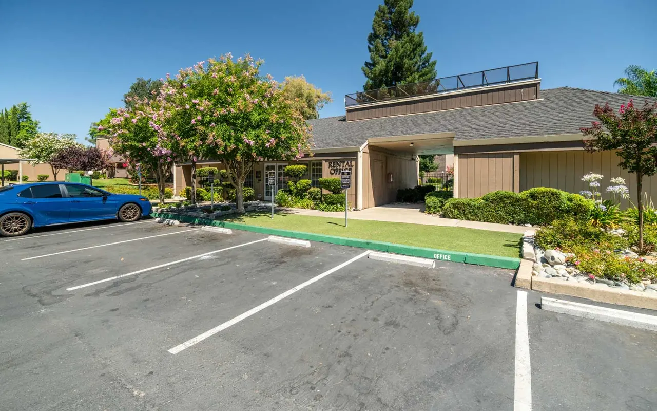 Exterior view of an apartment complex with a blue car parked and trees in bloom.