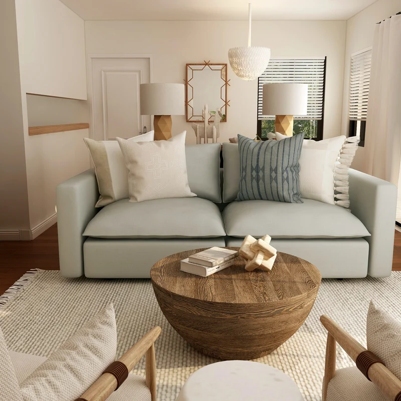Modern Living Room Design A stylish living room featuring a light blue sofa with multiple cushions, two armchairs, a round wooden coffee table, and neutral decor. The room has large windows with white curtains and a cozy, inviting atmosphere.