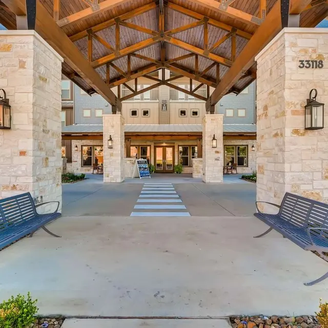 Entrance area of a modern apartment complex featuring a large wooden roof and benches.