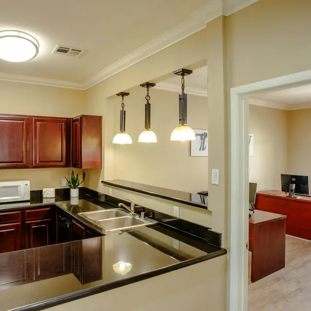Modern kitchen with dark wood cabinets, black countertops, and a view into a light office area with a desk.
