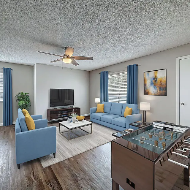 Cozy Modern Living Room A modern living room featuring blue couches with yellow cushions, a coffee table, a foosball table, and a television on a stand.