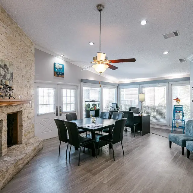 Cozy Modern Living Room A spacious, airy living room featuring a stone fireplace, a wooden dining table with chairs, and large windows letting in natural light.