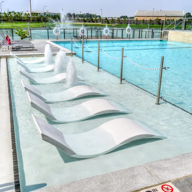 A modern pool area featuring submerged loungers and water jets, surrounded by clear water and safety equipment.