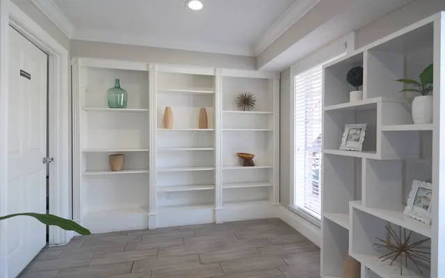 A modern living room featuring white shelves, decorative vases, and natural light coming through windows.
