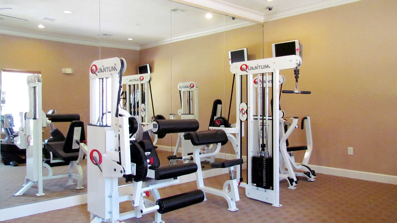 A gym area featuring multiple workout machines and equipment, with mirrors on the wall reflecting the surroundings.