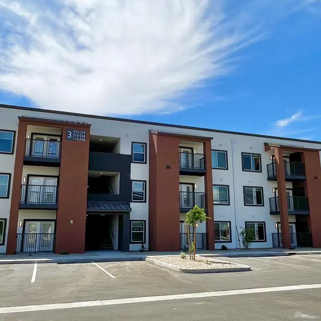 Modern Apartment Building A modern three-story apartment building with white and brick facade, featuring balconies and a clear blue sky in the background.