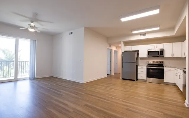 An open-concept interior of a modern apartment featuring a kitchen area with stainless steel appliances, a living space with wooden flooring, and large windows allowing natural light.